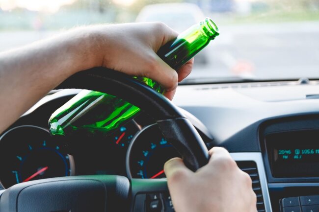 Drunk young man driving a car with a bottle of beer, facing DWI charges